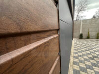 Garaż blaszany dwuspadowy 6 m x 5,8 m Orzech z bramą segmentową Grafit zbliżenie na strukturą blachy drewnopodobnej orzech